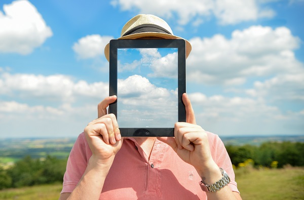 A Person Wearing Hat Holding a Tablet with Sky Image in Front of His Face
